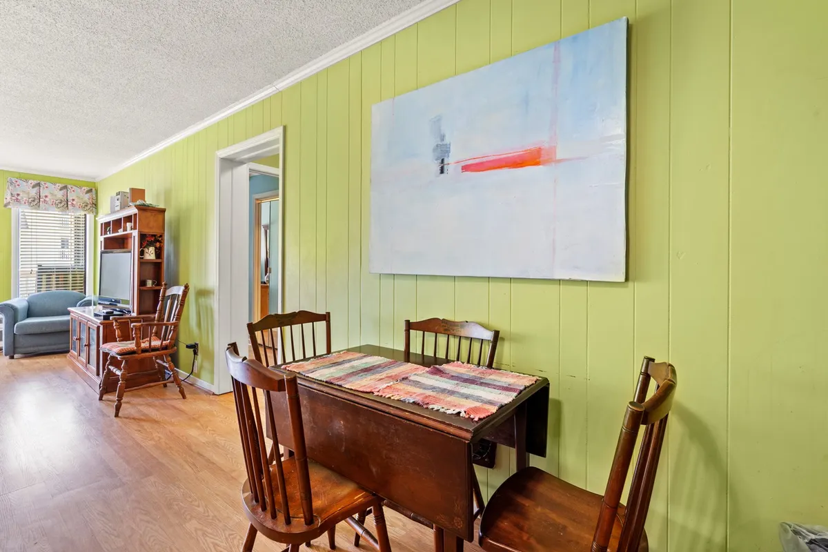 A dining area with a family-sized table, abstract art, and green walls. The setting is staged for family meals, gatherings, or intimate dinners, radiating a creative and communal vibe.