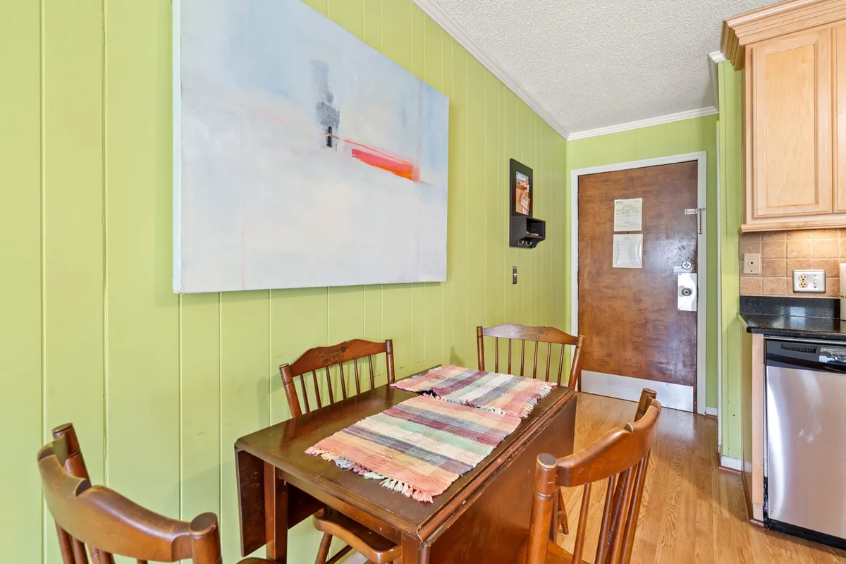 A cheerful dining area with a dining table set against a playful green wall adorned with colorful artwork. The space feels welcoming and lively, encouraging shared meals and casual gatherings amidst a creative, homey atmosphere.
