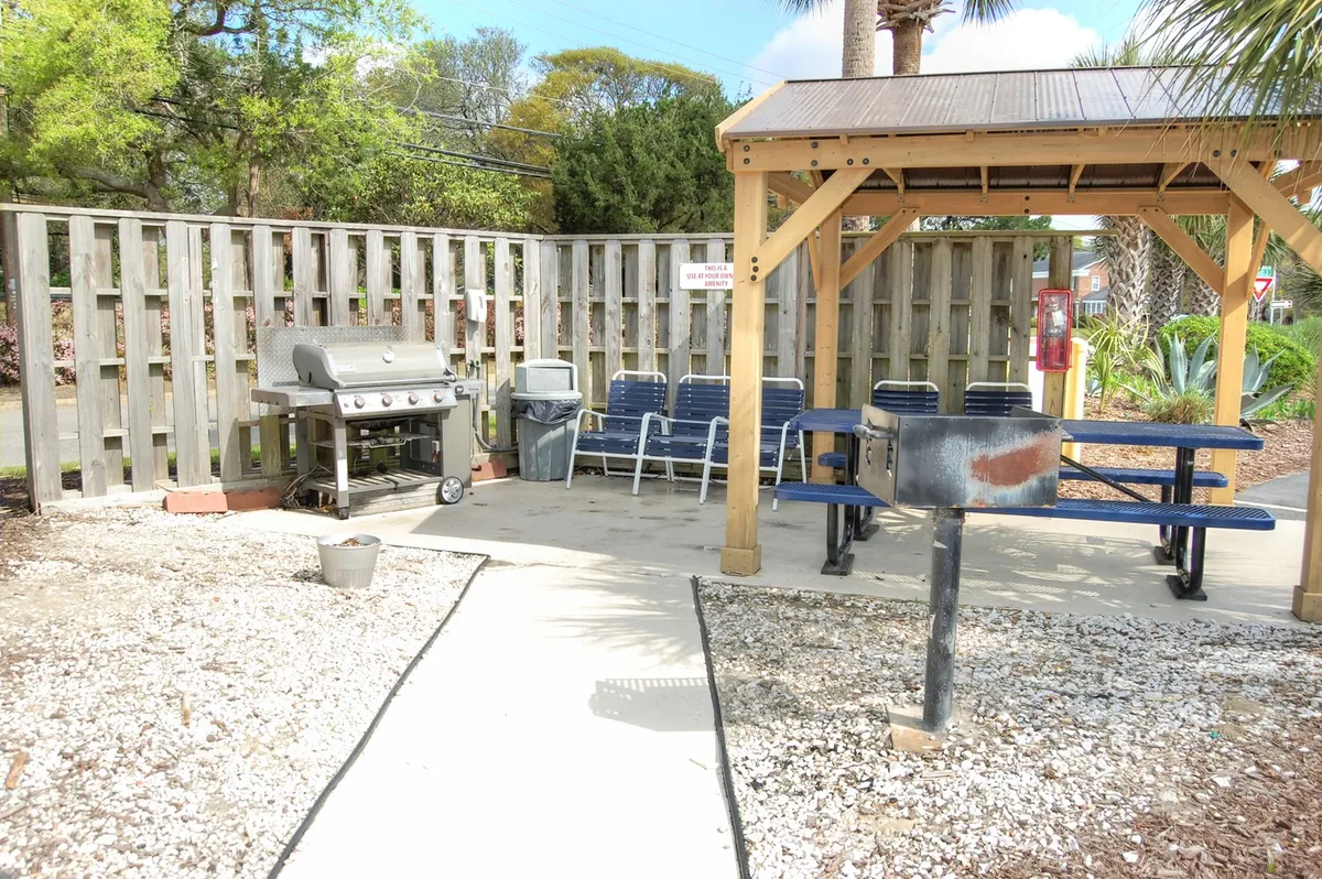 A cozy exterior area featuring a grill, picnic table, and casual seating surrounded by decorative stones. The scene hints at a communal atmosphere, ideal for barbecues, family gatherings, or relaxed afternoons spent outdoors.