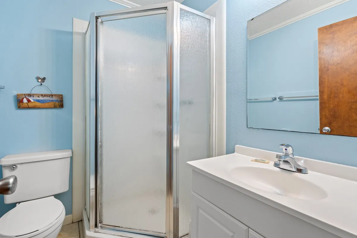 A serene and modern bathroom with a glass shower enclosure, vanity sink, toilet, and a large mirror. The atmosphere is clean and spa-like, perfect for morning or evening routines.