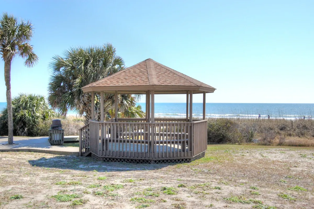 This image features a charming gazebo overlooking the ocean, surrounded by palm trees and a clear sky. The scene is tranquil, inviting visitors to relax, enjoy a morning coffee, or watch the sunset together. The setting feels intimate and perfect for couples or friends seeking a romantic or peaceful escape.