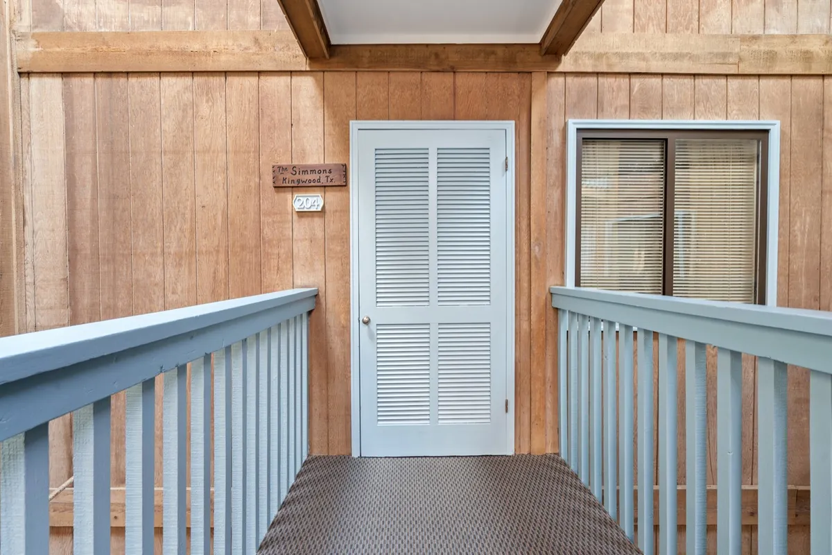 This inviting shot features a blue door framed by a wooden railing and a nameplate, welcoming guests as they enter the property. The entryway conveys a sense of arrival and sets the tone for the flexible, guest-friendly experience highlighted in the section.