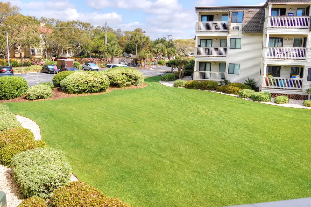 A well-maintained green lawn dotted with neatly trimmed shrubs frames the balconies of Ocean Forest Villas. The sun shines brightly, inviting guests to relax on the private balconies or enjoy social moments on the lush grass.