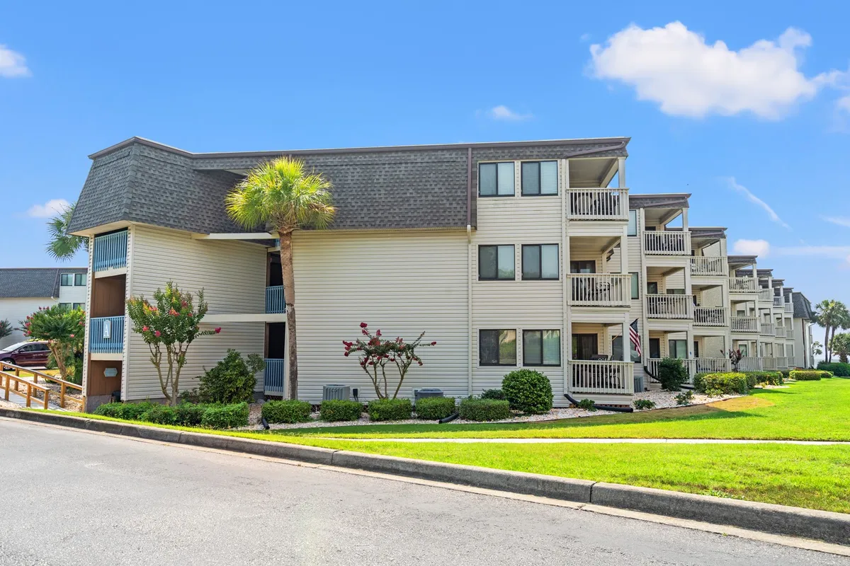 This exterior image showcases a welcoming condo building surrounded by well-maintained landscaped gardens, with balconies adorned with palm trees. Residents can be seen enjoying the outdoor spaces, relaxing on balconies, and strolling through the lush gardens.